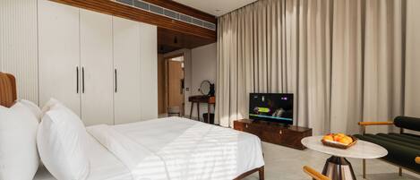 A modern hotel room with a large bed, a TV, a dining table, and a sofa.