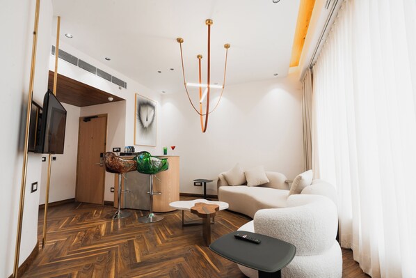 A modern living room with a sofa, a coffee table, a TV, and a unique green chair. - AVA Hotel Chandigarh Zirakpur (Dera Bassi)