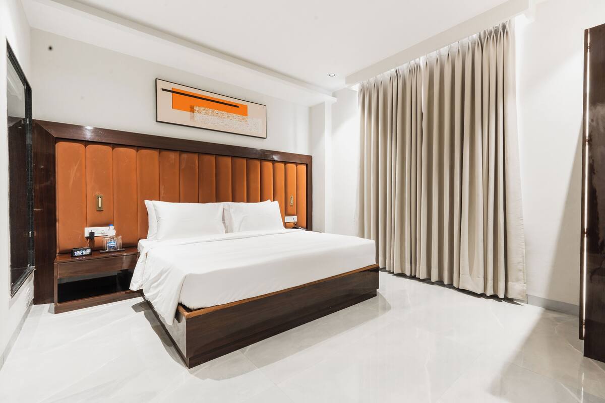 A modern hotel room with a large bed, wooden headboard, and a nightstand with a clock.