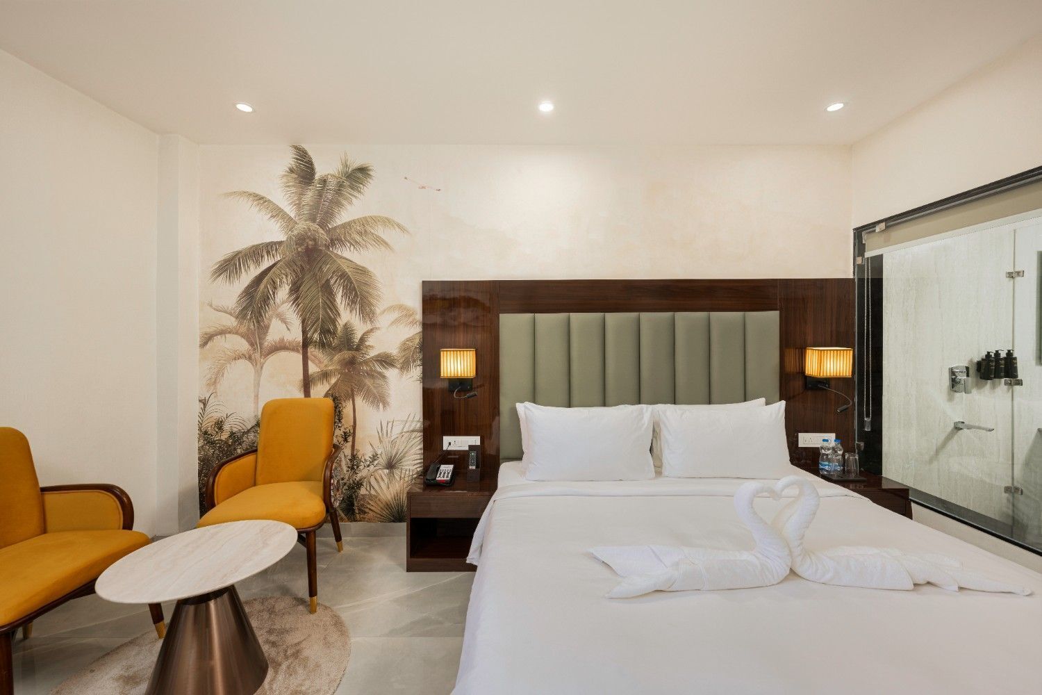 A hotel room with a bed, two chairs, a nightstand, a wall-mounted lamp, and a large window.