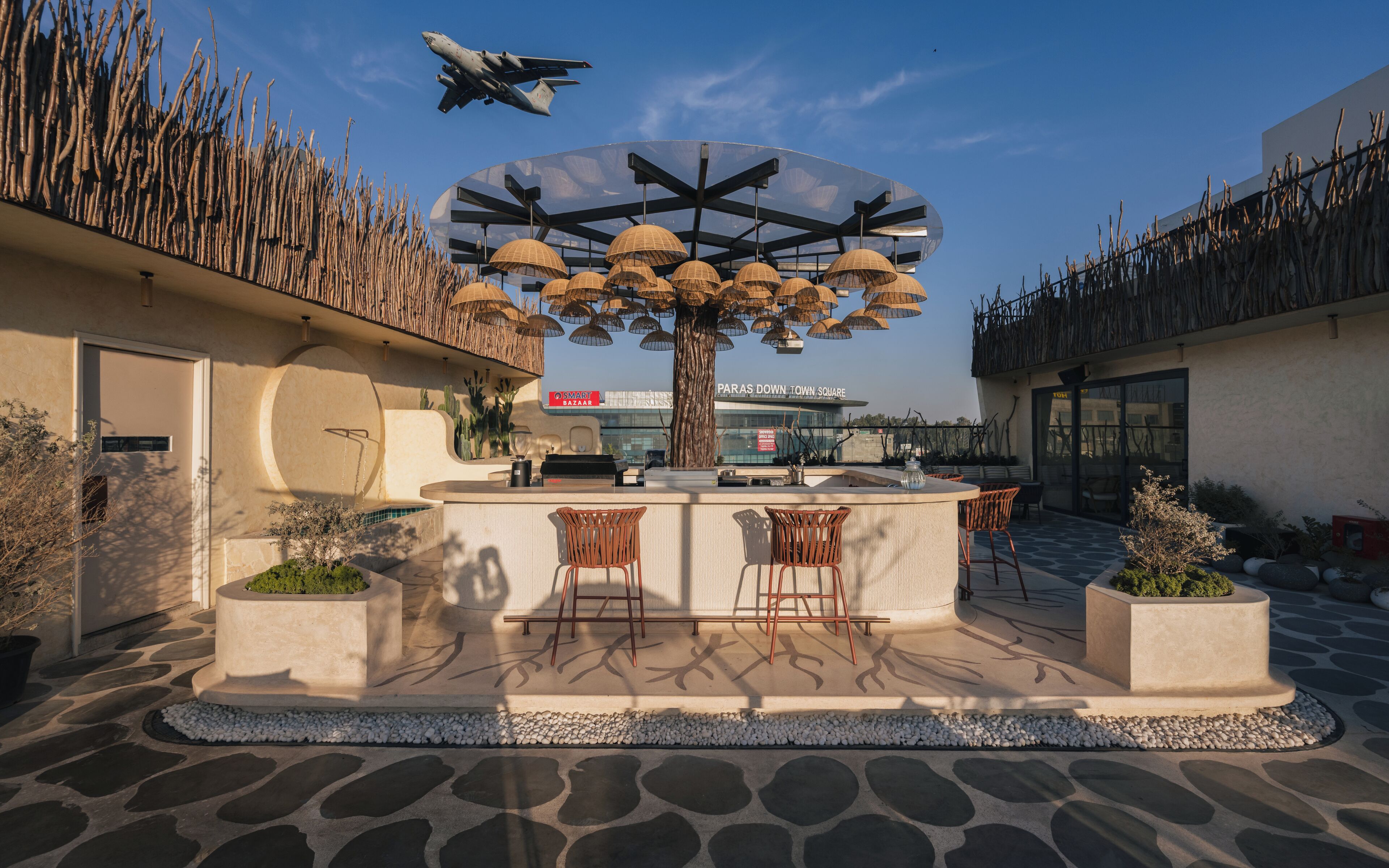 Un área de estar al aire libre con un árbol central, un bar y vistas a un edificio en el fondo.