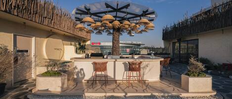 Un área de estar al aire libre con un árbol central, un bar y vistas a un edificio en el fondo.