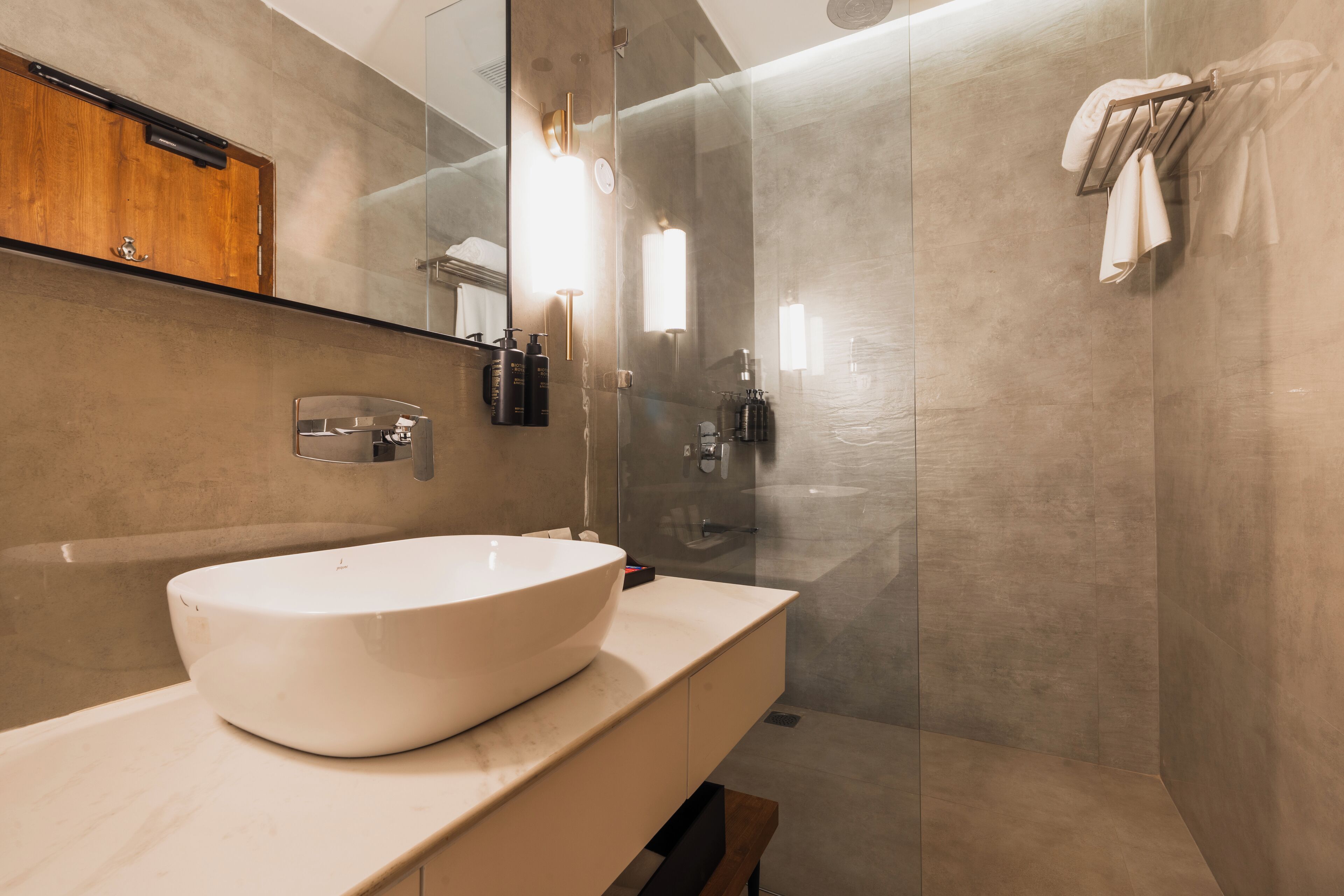 A modern bathroom with a large white sink, a glass shower enclosure, and a wooden vanity.