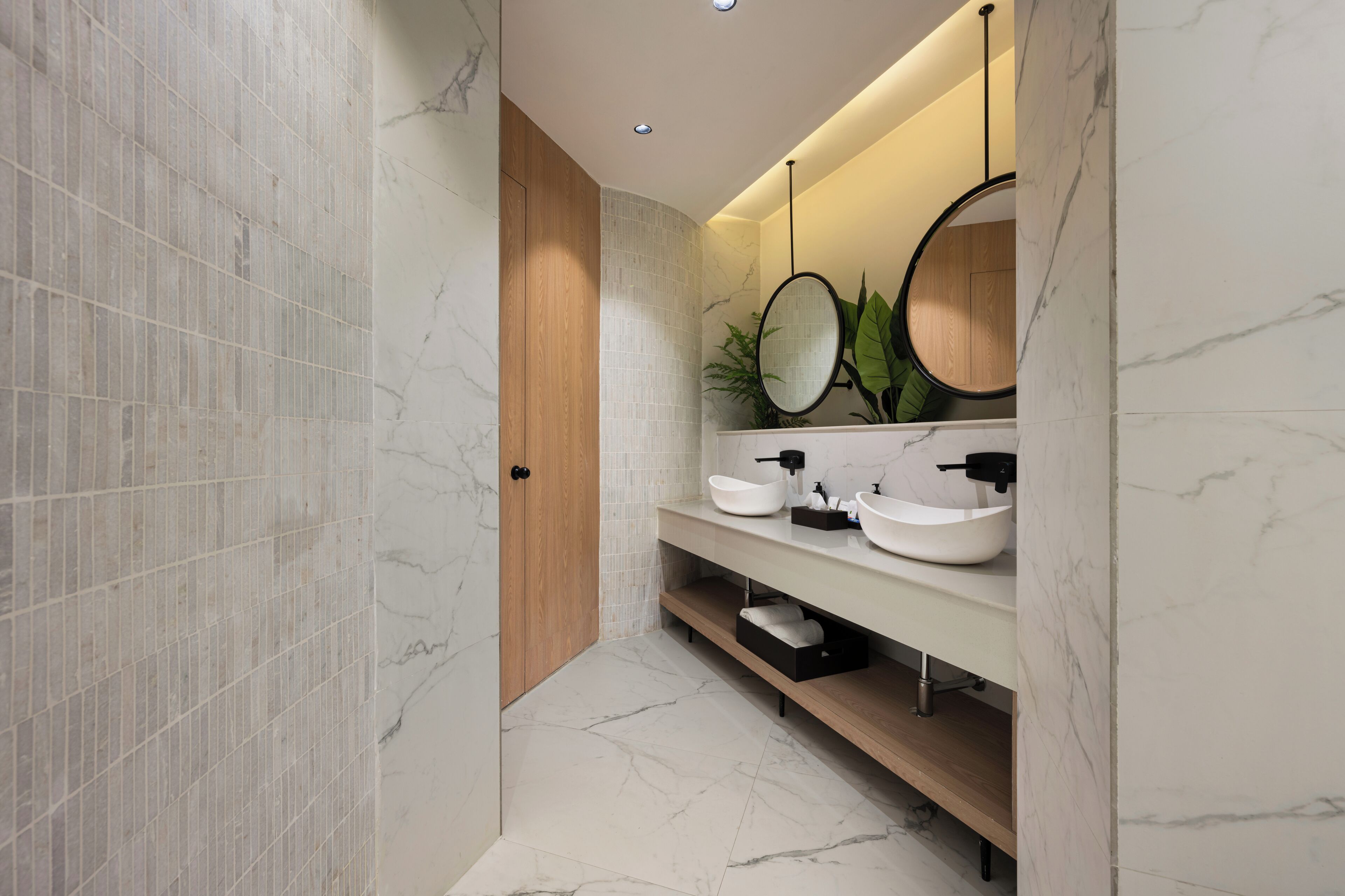 Une salle de bain moderne avec un sol en marbre, une porte en bois et un meuble-lavabo doté de deux vasques et d’un miroir.