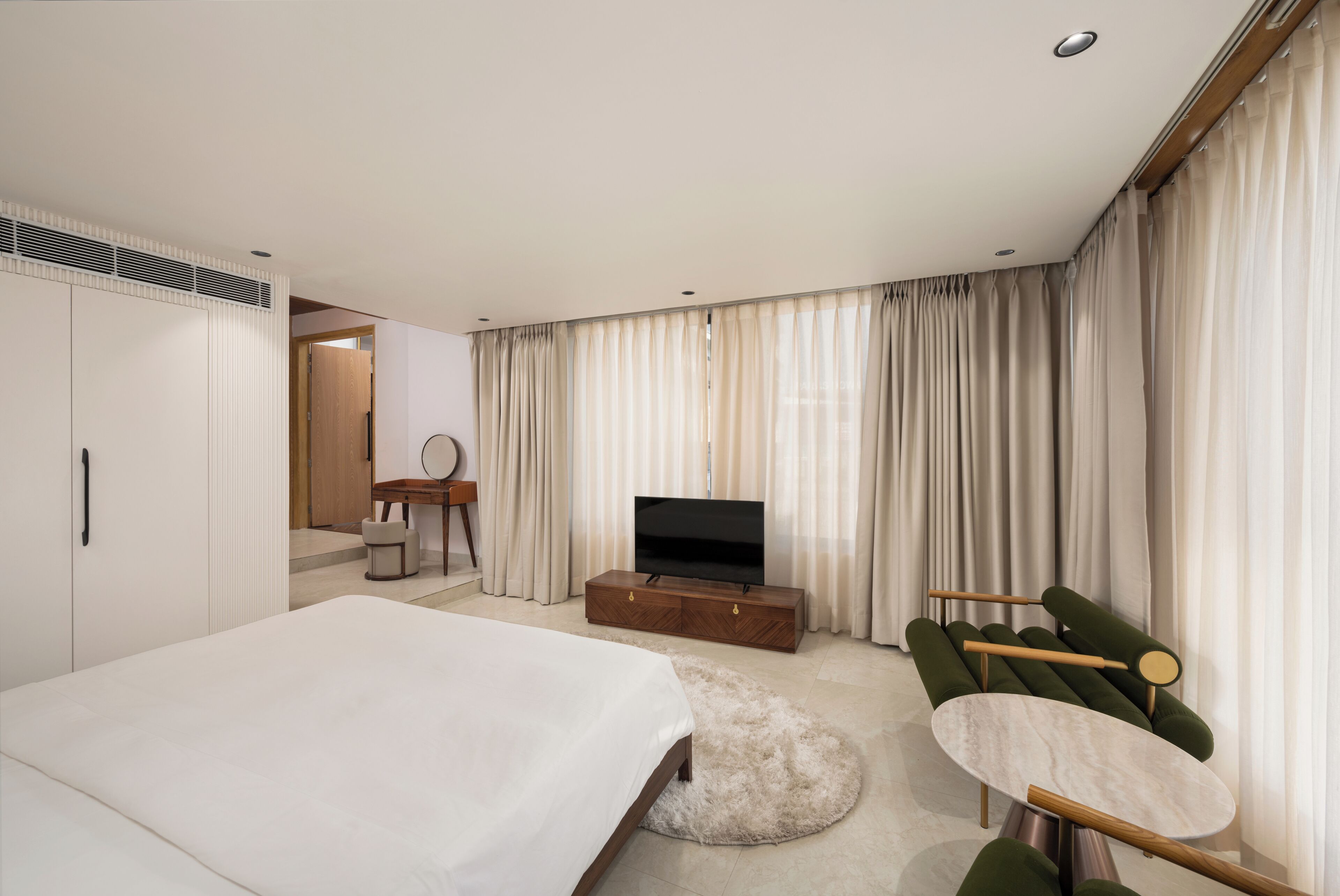 A modern hotel room with a large bed, a TV on a wooden stand, a green sofa, and a small table.