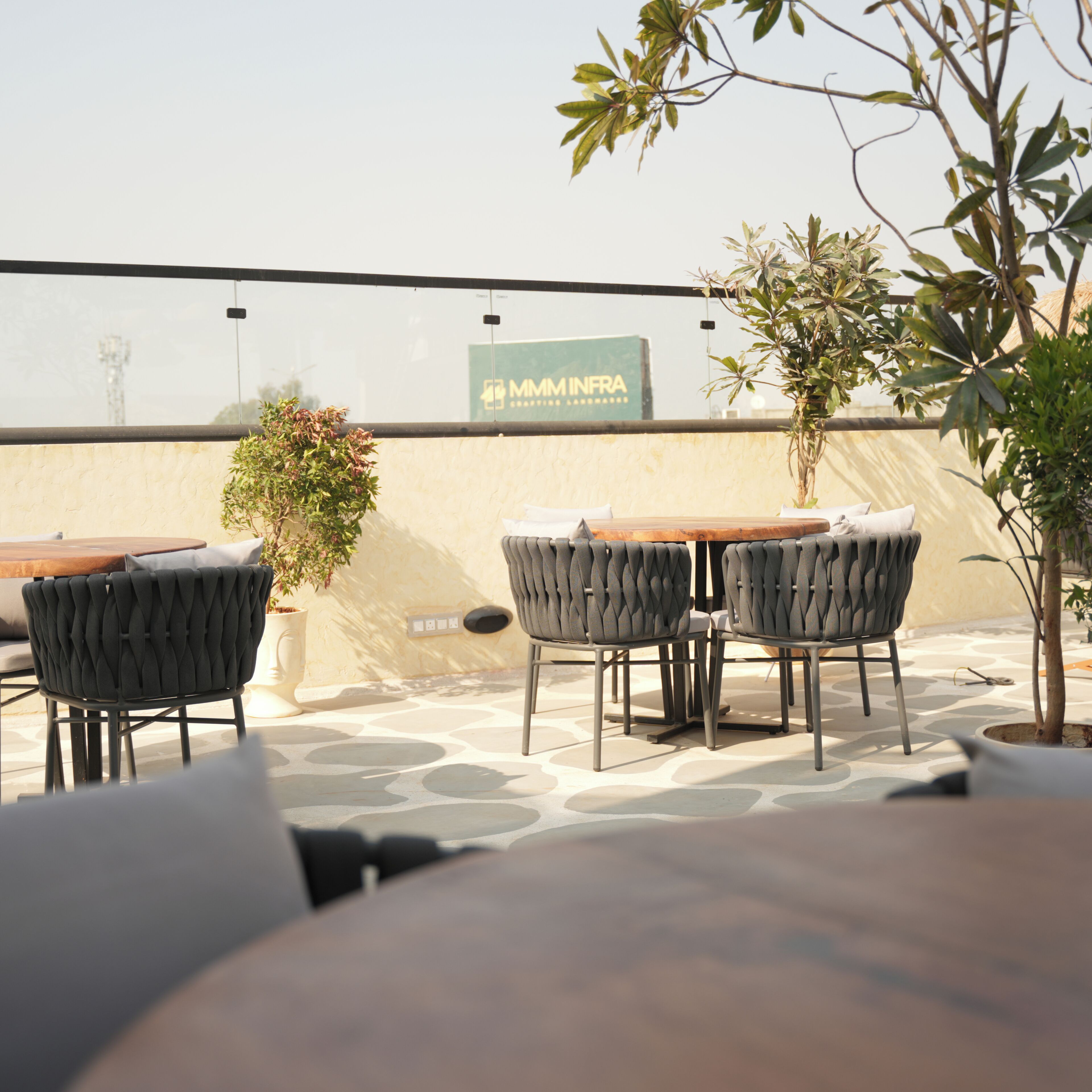 An outdoor seating area with a table and chairs, a potted plant, and a view of a building with a sign.