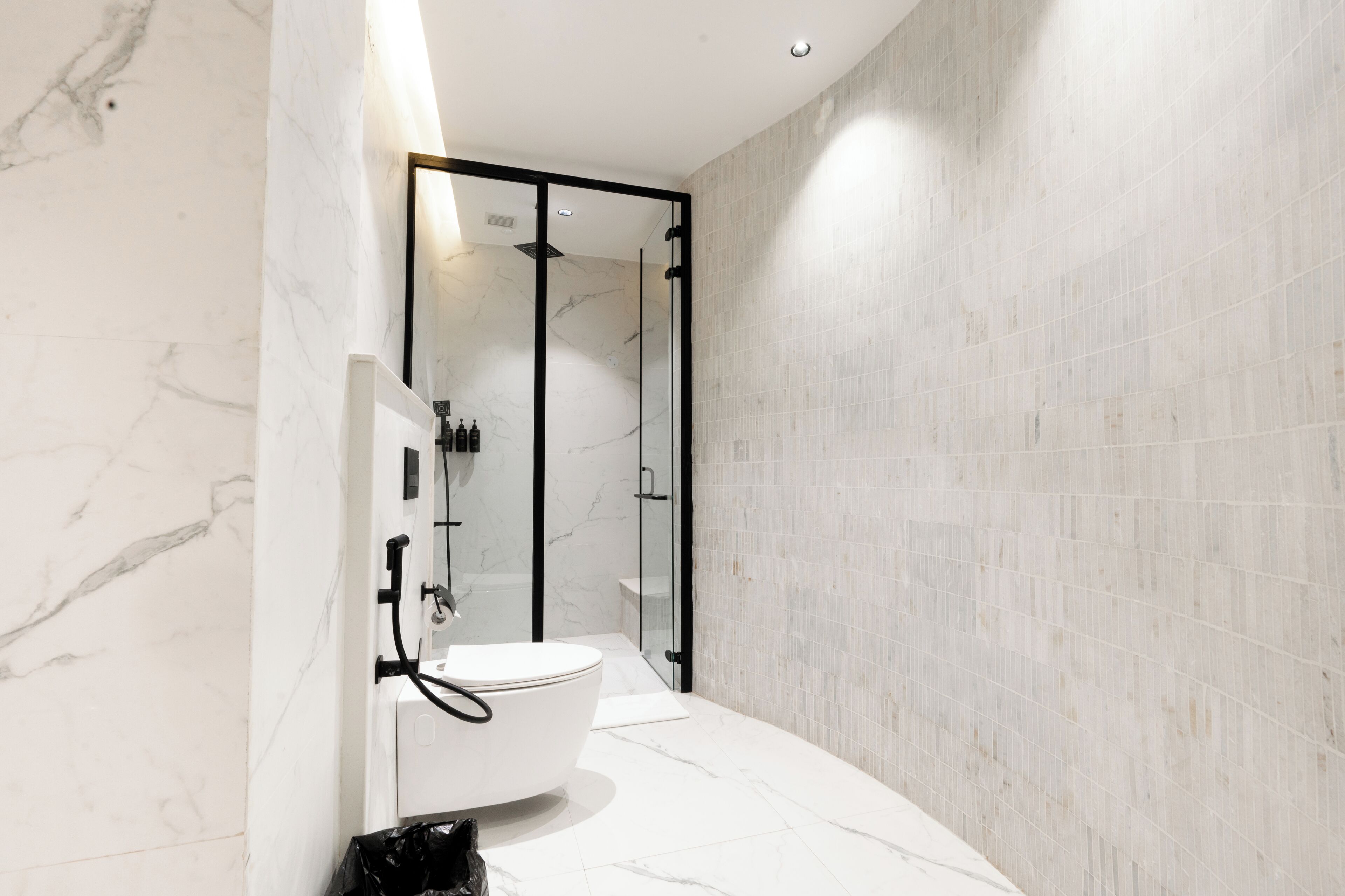 A modern bathroom with a glass-enclosed shower, a white toilet, and marble walls.
