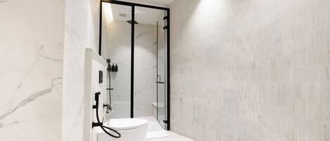 A modern bathroom with a glass-enclosed shower, a white toilet, and marble walls.