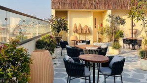 A rooftop terrace with outdoor seating, a thatched roof, and potted plants. - AVA Hotel Chandigarh Zirakpur (Dera Bassi)