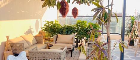 A rooftop terrace with wicker furniture, a potted plant, and a hanging decoration.
