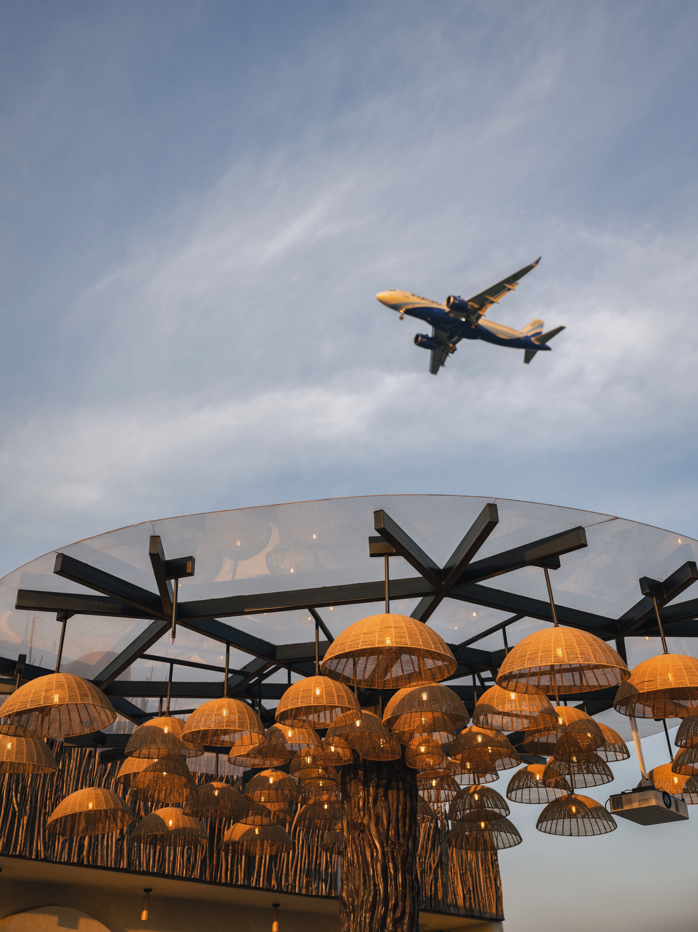 Ein Flugzeug fliegt am Himmel über einer Struktur mit mehreren hängenden Lampen.