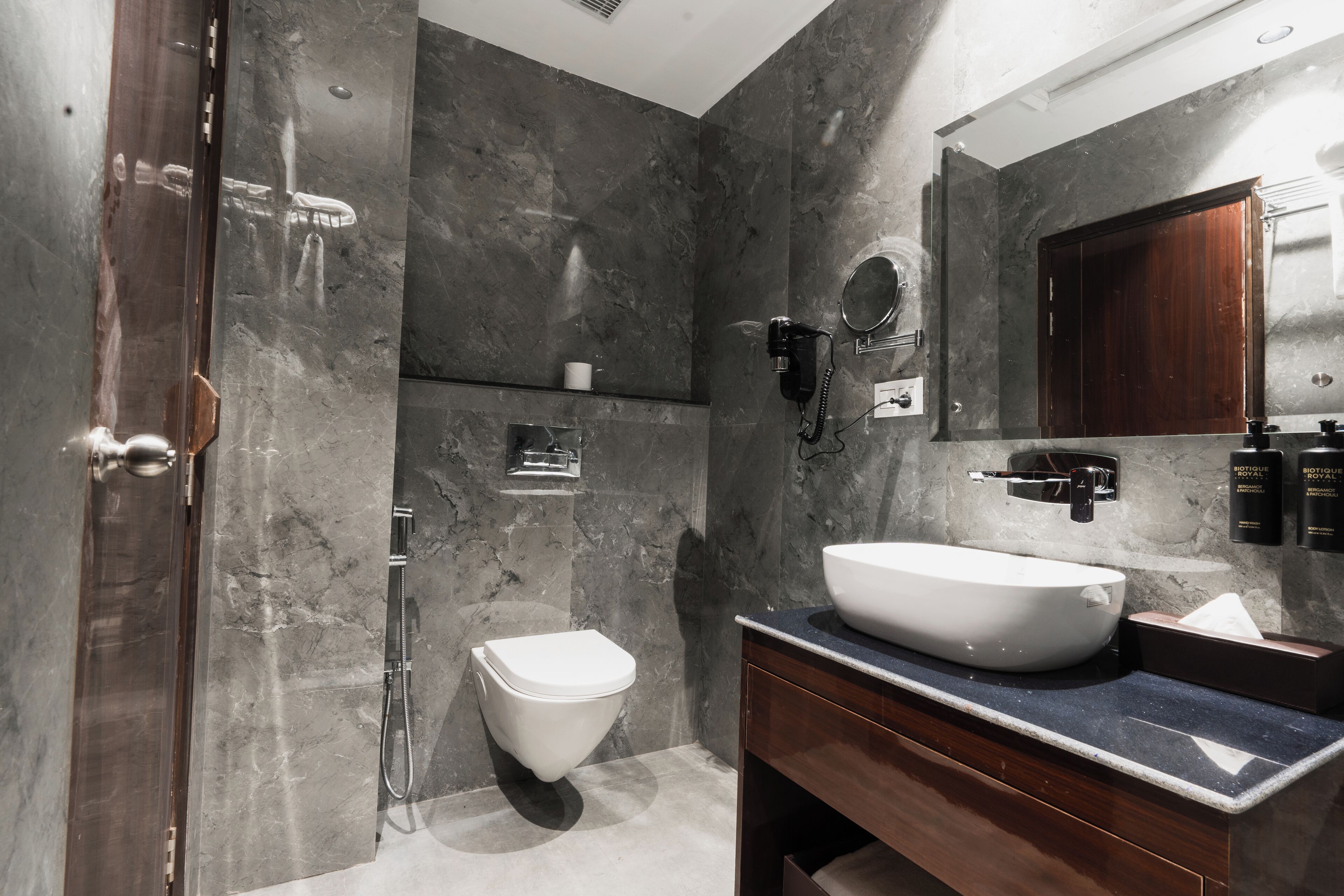 A modern bathroom with a large marble wall, a white sink, and a wooden vanity.