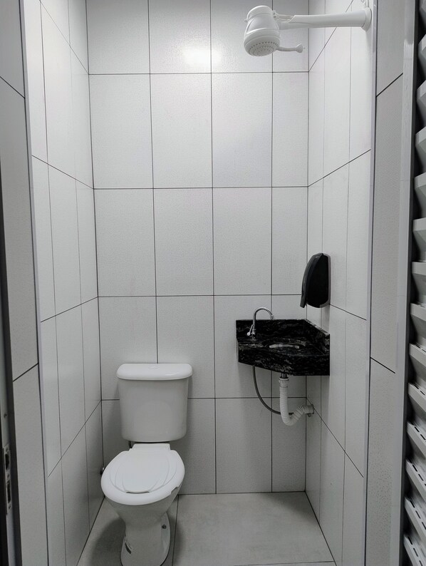 A small, modern bathroom with a white toilet, a black marble sink, and a handheld showerhead.