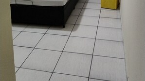 Una habitación pequeña y limpia, con una cama individual, paredes blancas y suelo de baldosas.