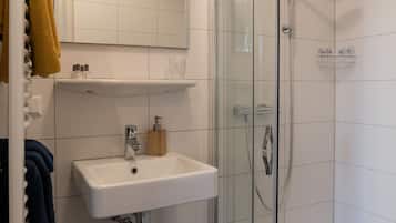 A modern bathroom with a glass-enclosed shower, a white sink, and a mirror above it.