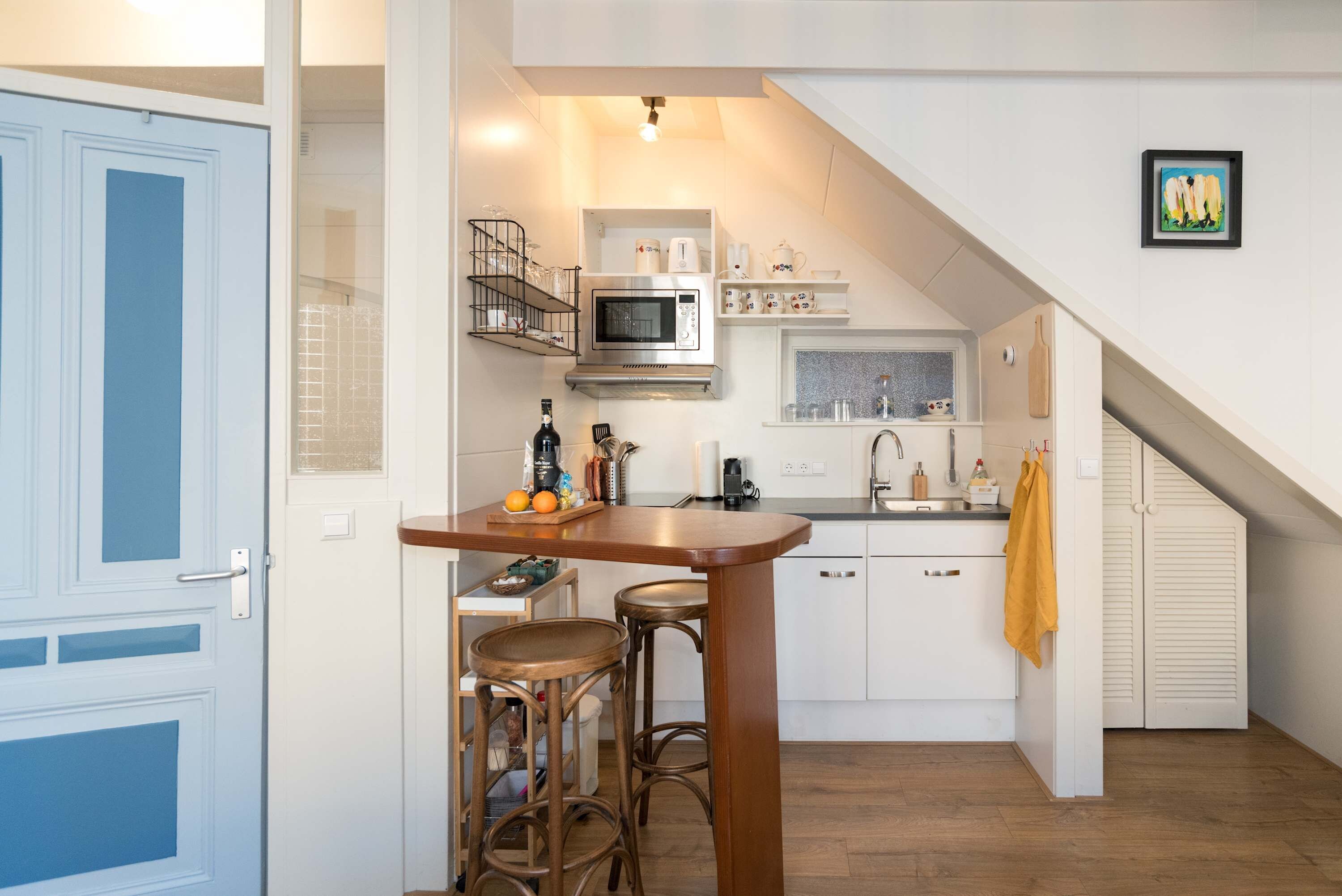 A compact kitchen with a microwave, sink, and bar stools.