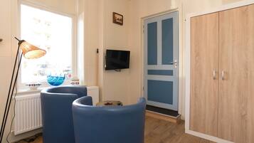 A room with a large window, a television, a wardrobe, and two blue chairs.