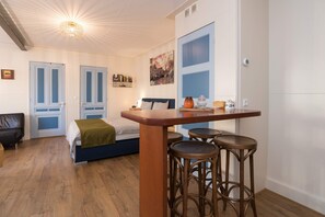 A compact room with a bed, a small table, and two bar stools. There is a door with a blue frame and a painting on the wall. - Luttik Oudorp 30B Apartment Alkmaar (Alkmaar)
