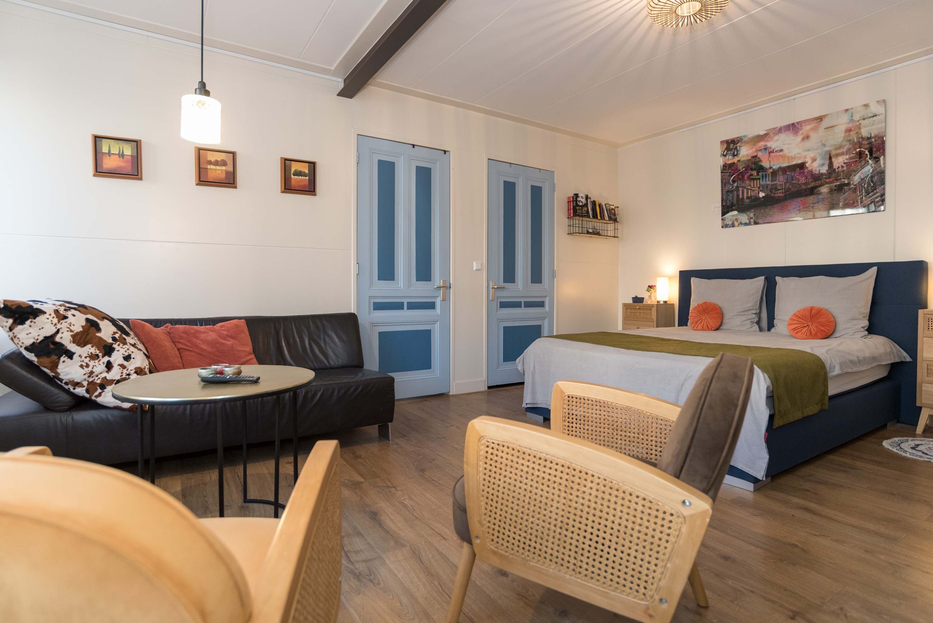 Een knus ingerichte kamer met een bank, een klein rond tafeltje, een bed met oranje kussens en een houten stoel.