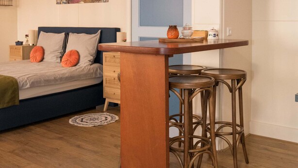 Um espaço de estar compacto com cama, uma pequena área de jantar com banquetas e uma prateleira fixada na parede.