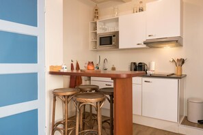 Una cocina compacta con una isla central, taburetes de bar, microondas y un fregadero.