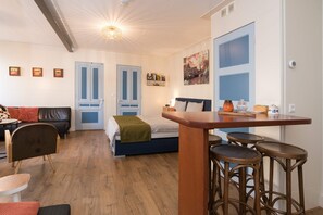 Un espacio habitable compacto con cama, sofá, mesa de comedor con taburetes y una zona de kitchenette.