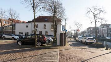 Une vue de rue avec des voitures garées, un canal et des bâtiments à l’architecture traditionnelle.