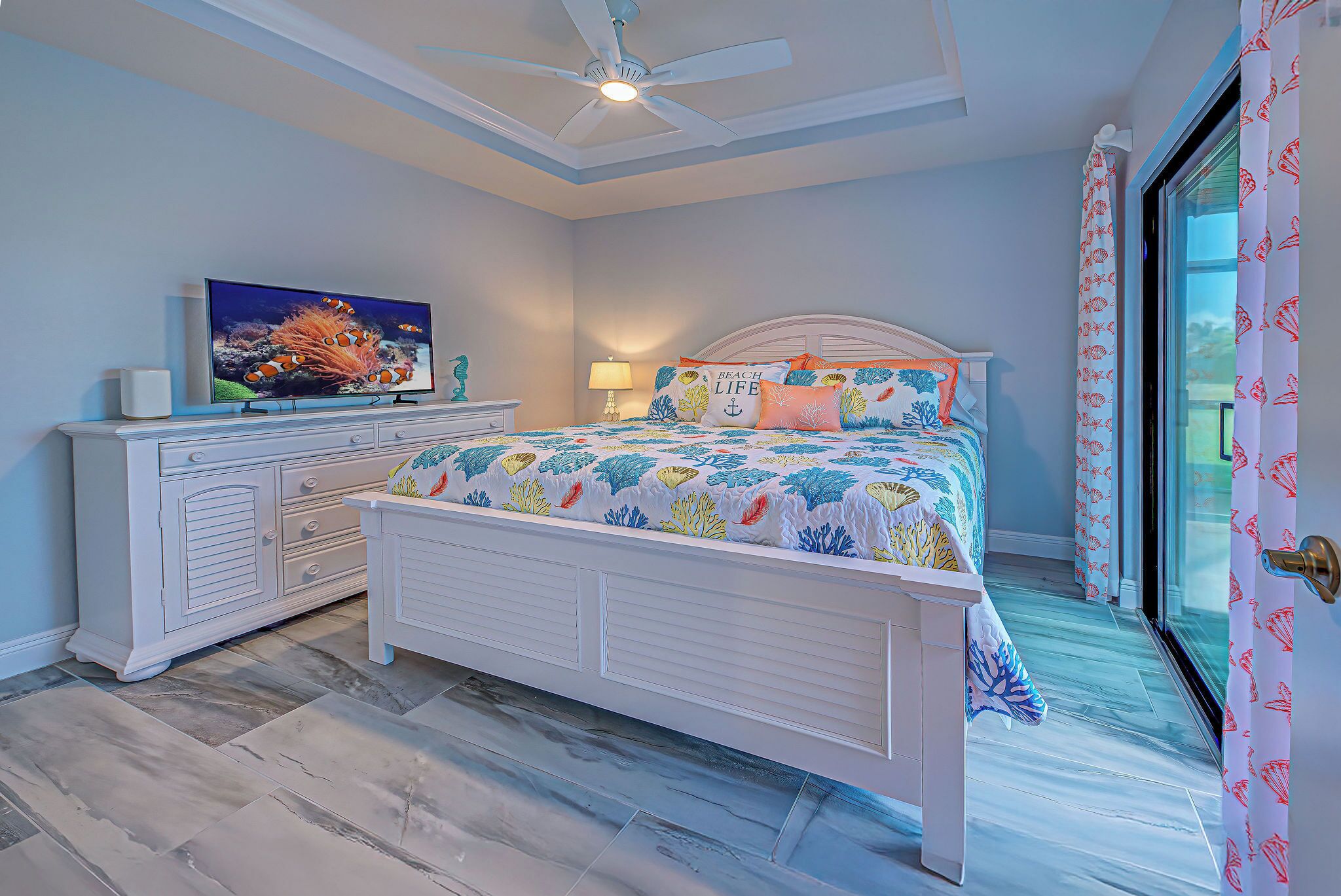 A bedroom with a bed, a TV, a dresser, and a window with curtains.