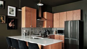 A modern kitchen with wooden cabinets, a stainless steel refrigerator, a white countertop, and bar stools. - Dreamy Condo with Fireplace, Rooftop, Gym, Parking  |  Sleeps 5 w/ King Bed, Sleeper Sofa, Hidden Bunk, Shared Rooftop and Gym, Free Dedicated Parking, Minutes to Broadway, Five Points & Grand Ole Opry, 24 Hr Hospitality (Nashville)