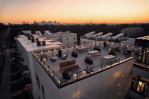 Terraza en la azotea con mobiliario exterior, unidades de aire acondicionado y el horizonte de la ciudad al atardecer.