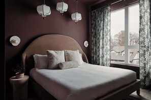 Un dormitorio con una cama grande, una mesita de noche con una planta y una ventana con cortinas.