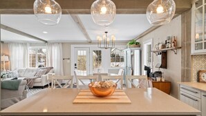 Una cocina amplia con una isla central, luces colgantes y vistas al comedor.