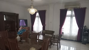 A dining area with a wooden table and chairs, a chandelier, and purple curtains. - Graha Dinar Hotel by HIMA (Cisarua)