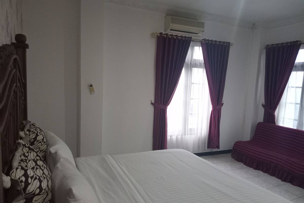 Une chambre à coucher avec un lit, un canapé et deux fenêtres avec des rideaux.