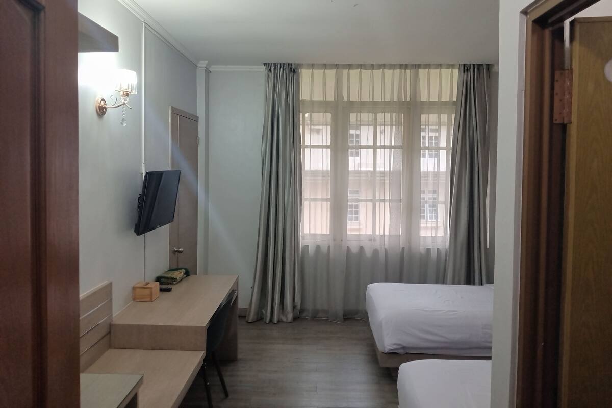 Une chambre d’hôtel avec un lit, un bureau, une télévision et une fenêtre avec des rideaux.