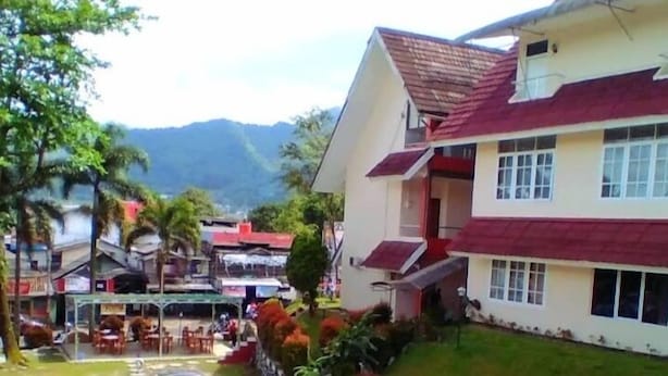 A two-story building with a red roof and white walls, surrounded by greenery and a mountainous backdrop. - Graha Dinar Hotel by HIMA (Cisarua)
