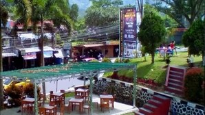 An outdoor seating area with tables and chairs, a covered patio, and a stone wall. - Graha Dinar Hotel by HIMA (Cisarua)