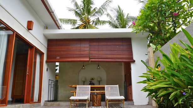 Un'area piscina con due poltrone in rattan bianco, un tavolo di legno e un soffitto in legno.