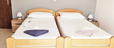 Une chambre double avec deux lits en bois, chacun muni d’une table de chevet, d’une lampe et d’une serviette pliée.