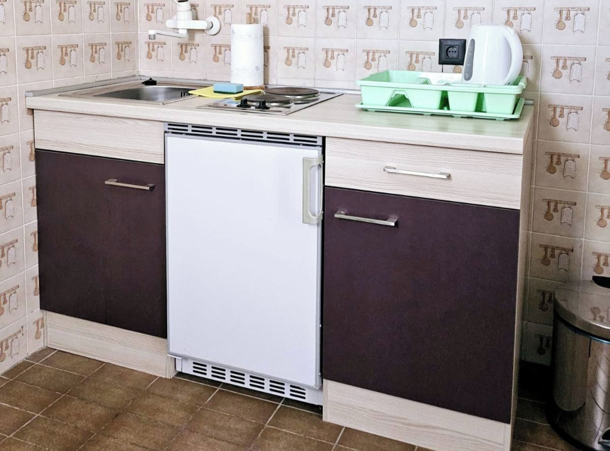 Uma cozinha compacta com geladeira embutida, pia e bancada com chaleira e escorredor de louça verde.