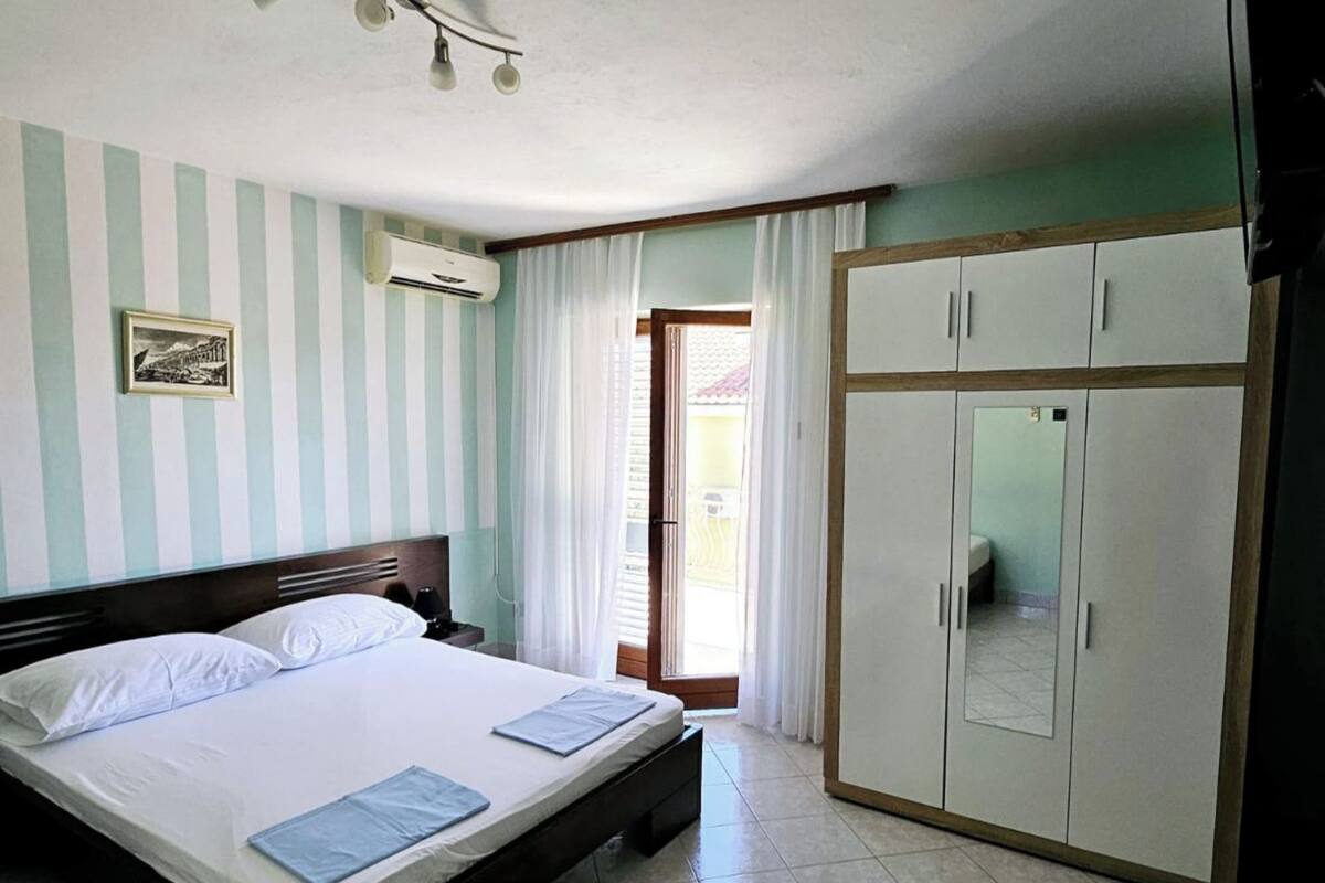A bedroom with a bed, a wardrobe, a nightstand, and a window with curtains.