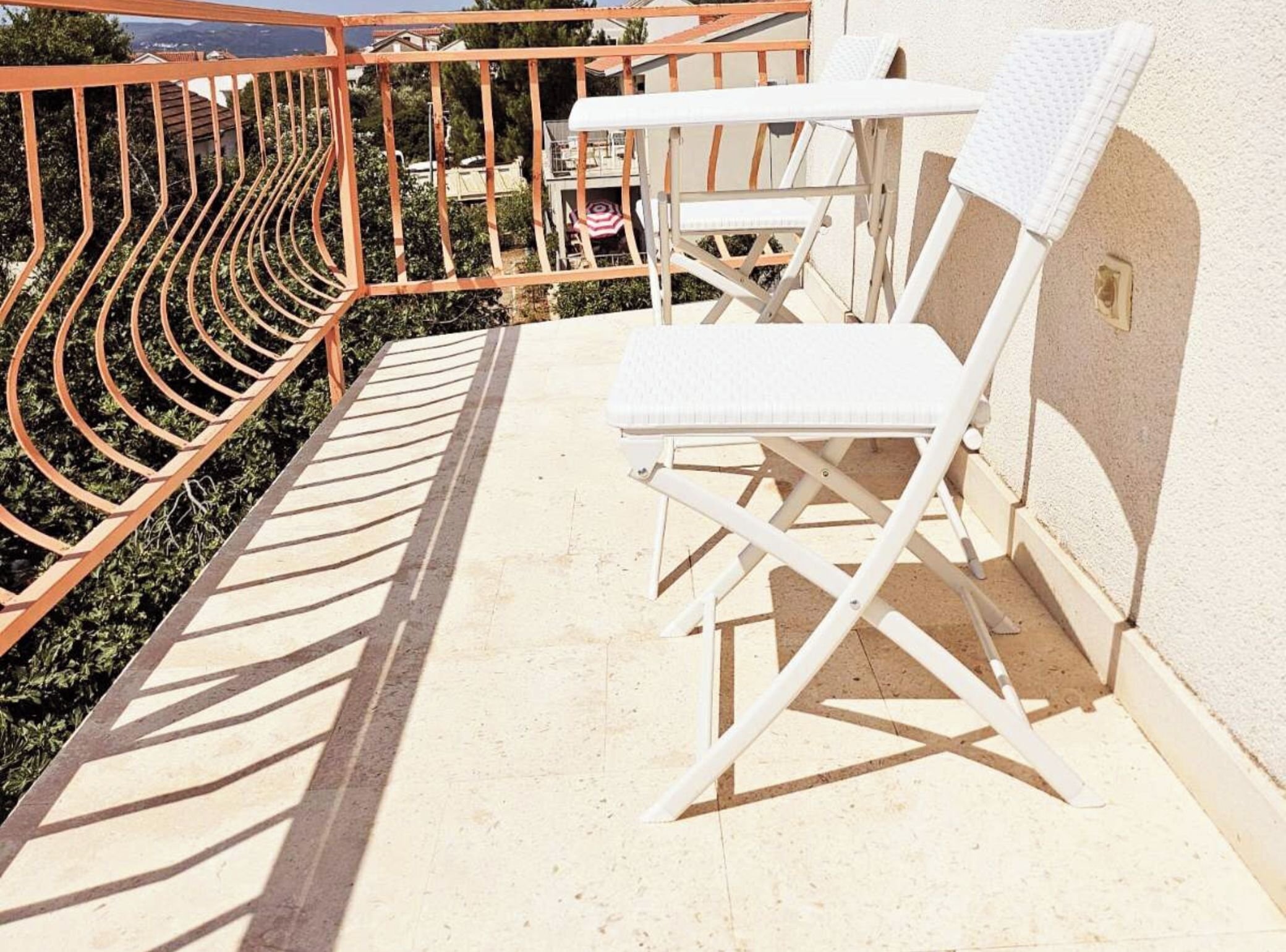 A balcony with a white chair and a small table, surrounded by a metal railing.