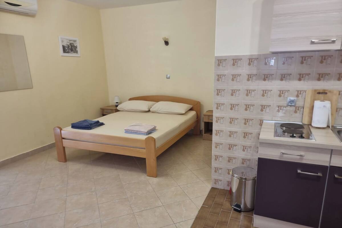 A bedroom with a wooden bed, a nightstand, a wall-mounted air conditioner, and a small bedside table.