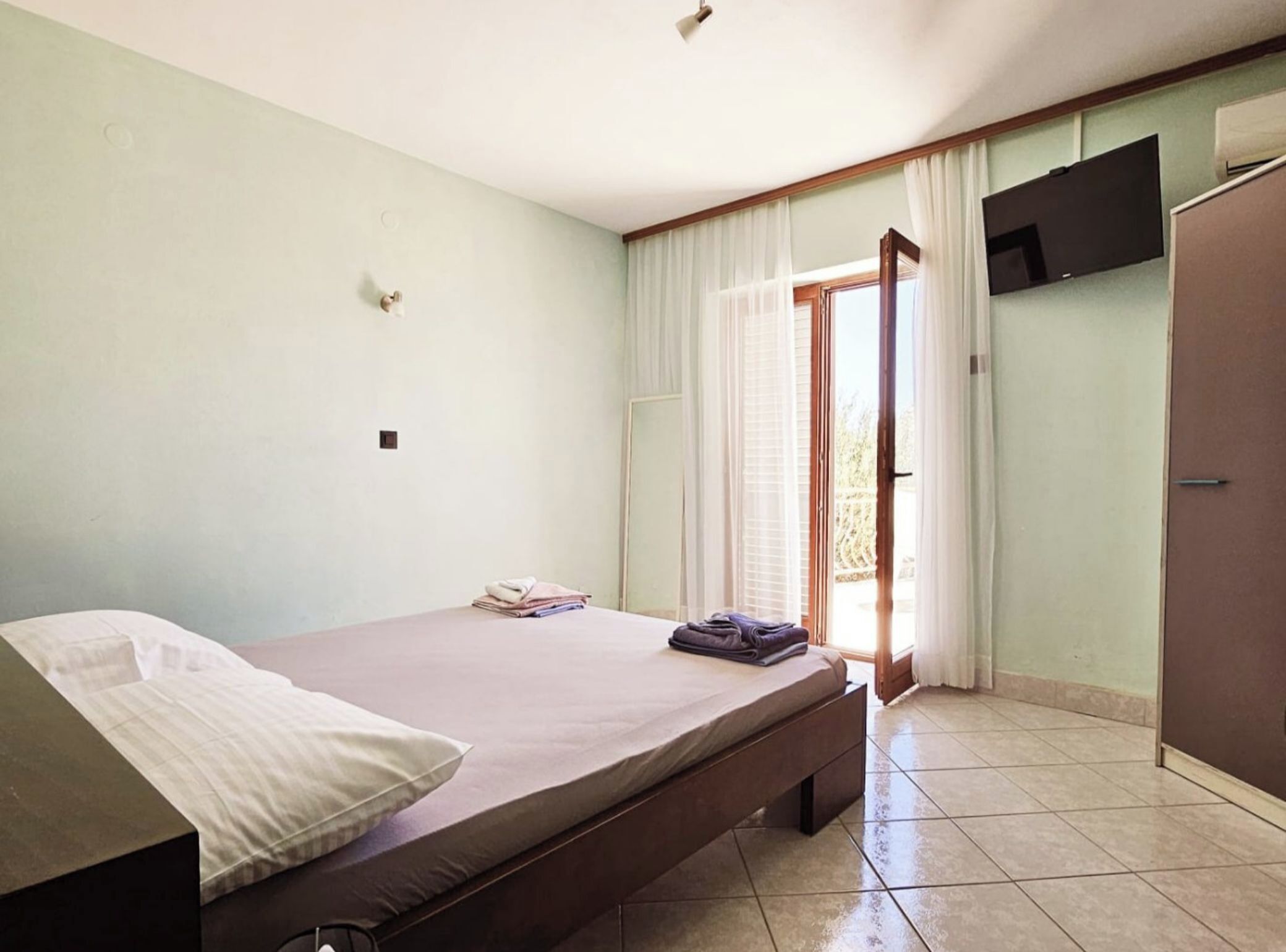 Quarto com cama, TV fixada na parede e porta que dá para o exterior.