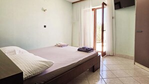 Une chambre à coucher avec un lit, un téléviseur fixé au mur et une porte donnant sur l’extérieur.
