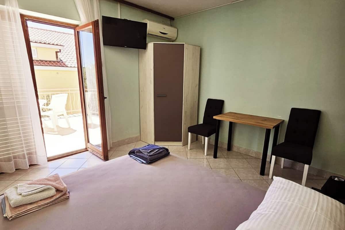 A hotel room with a bed, a desk, two chairs, a television, and an air conditioning unit.