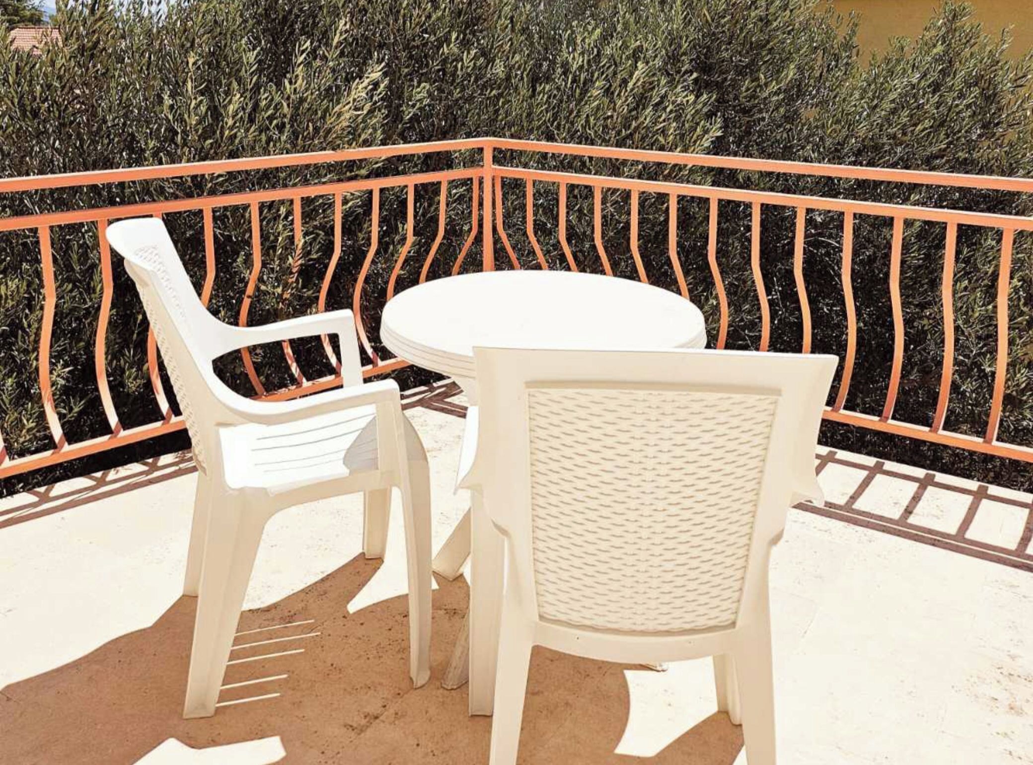 A balcony with a white table and two white chairs, surrounded by a metal railing.
