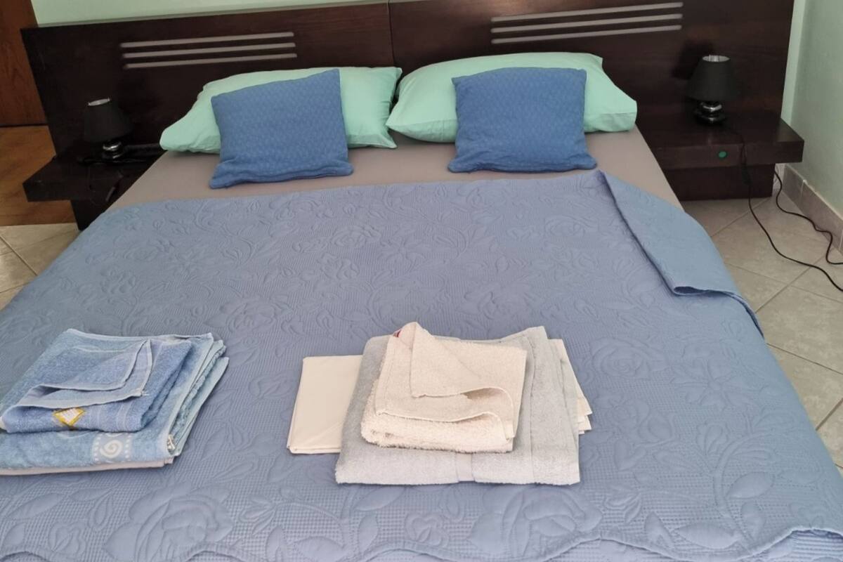 A neatly made bed with a blue bedspread, two pillows, and folded towels.