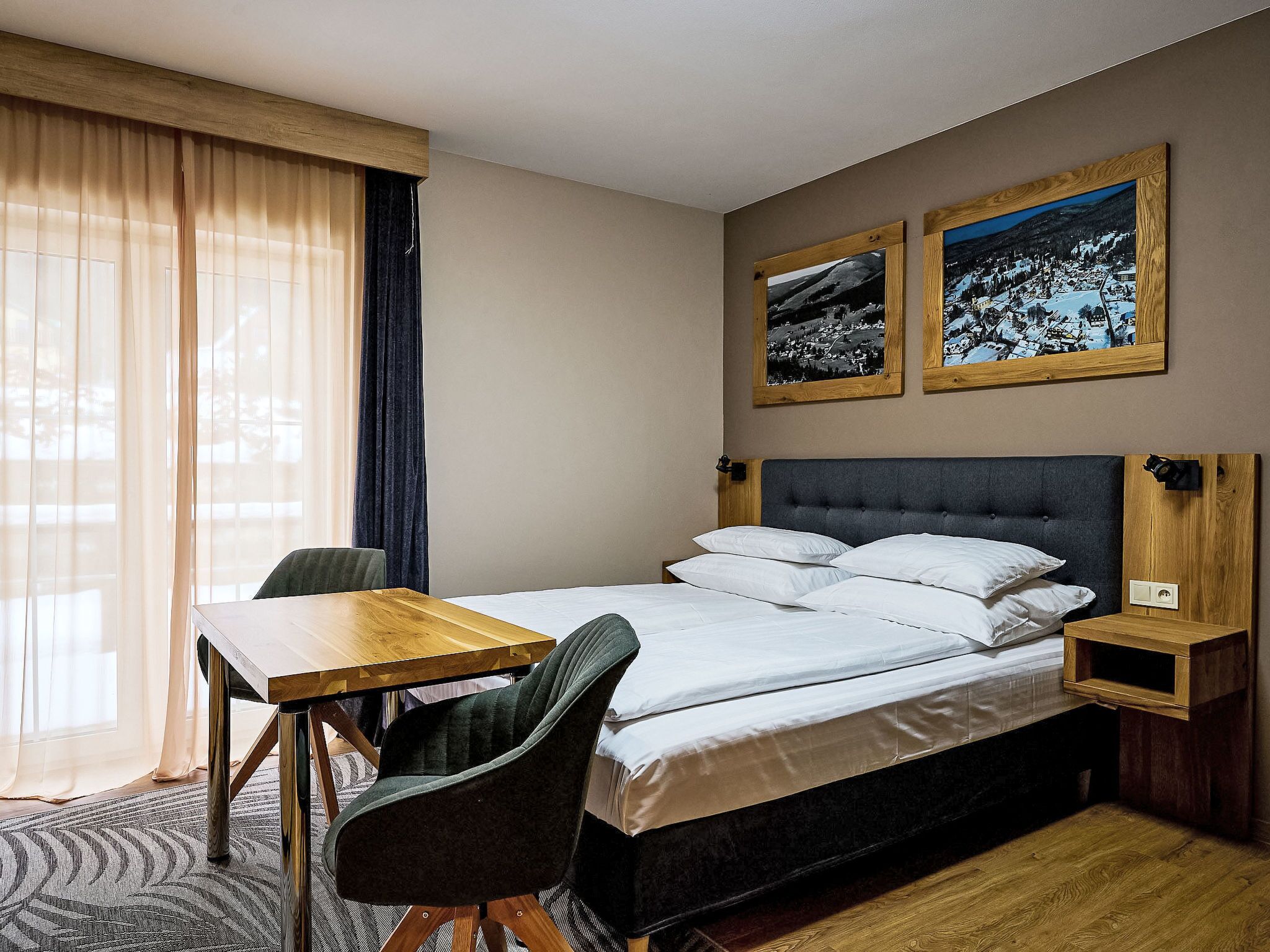 Une chambre d’hôtel avec un lit, un bureau en bois, une chaise et deux tableaux encadrés au mur.
