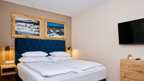 Uma cama bem arrumada com lençóis brancos, cabeceira azul e duas fotografias emolduradas acima.